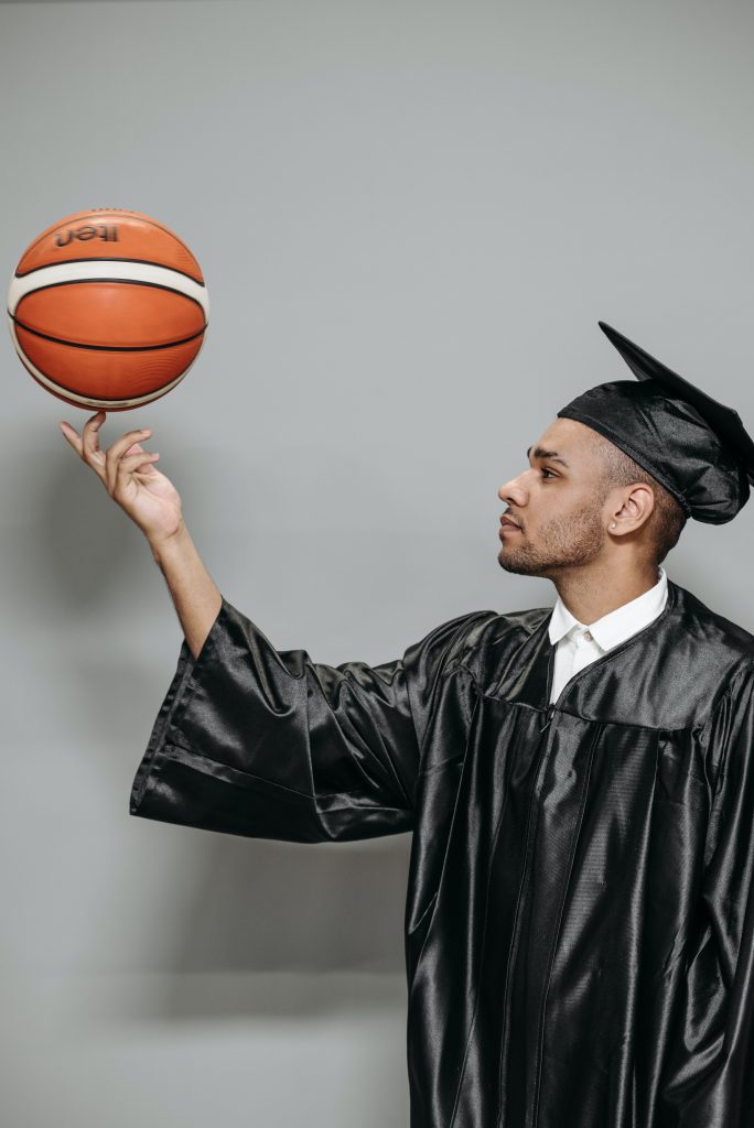 image of young basketball athletes with black cap & gown spin a basketball on his right hand middle finger.